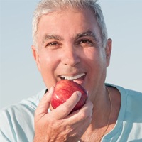 Smiling older man eating red apple with all-on-4 dental implant denture