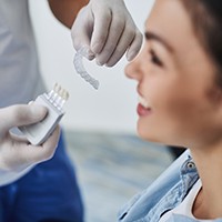 A dental professional holding an Invisalign aligner while a female patient smiles