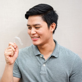 man smiling holding an Invisalign tray
