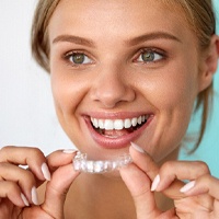 A woman smiling and holding a clear aligner.