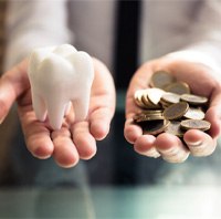 Hands holding a false tooth model and a bundle of coins 
