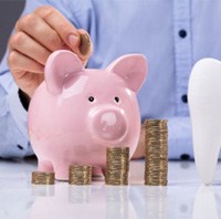 A white tooth beside a man inserting a coin into a piggy bank 