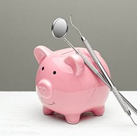 two dental instruments leaning against a pink piggy bank 