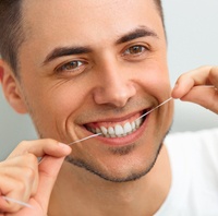 man smiling while flossing teeth to preventive dental emergency