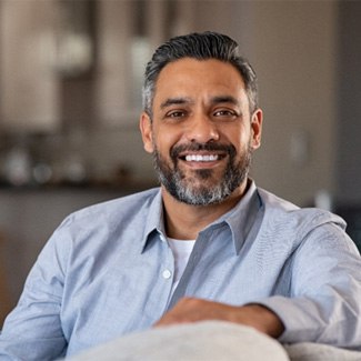 Man in blue shirt smiling on couch at home.