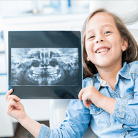 Smiling girl in dental chair holding x-rays