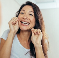 woman flossing in bathroom mirror