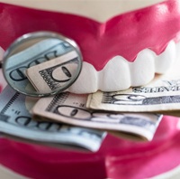 A mold of a mouth biting down on money and a dental mirror