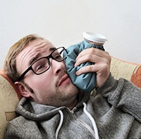 man lying down and holding a cold compress to his cheek 