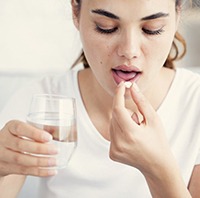 woman taking a pain medication pill with a glass of water 