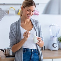 woman standing in her kitchen eating yogurt 