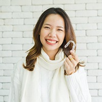 young woman in white sweater holding Invisalign aligner