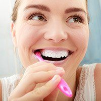 young woman with porcelain veneers brushing teeth