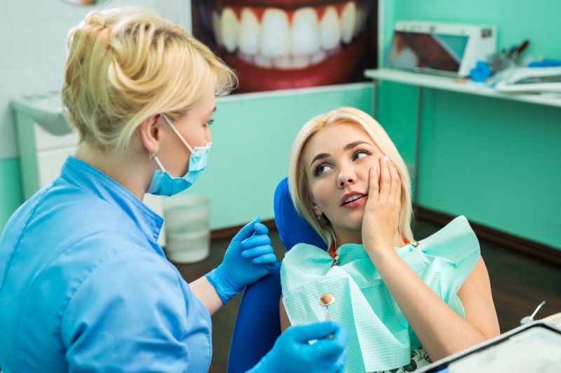 a woman holding her cheek in pain at the dentist office