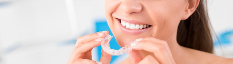 young woman smiling inserting Invisalign aligner