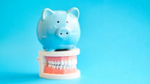 Blue piggy bank of dental insurance sitting on model teeth