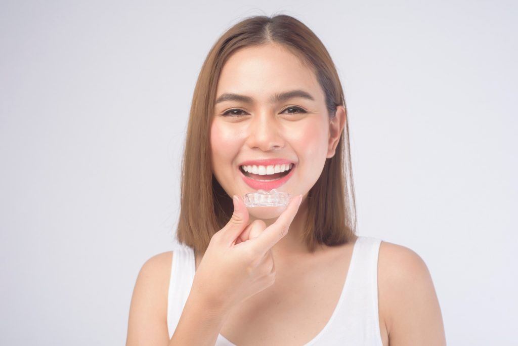 Woman smiling while holding Invisalign aligner