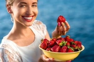Smiling young woman holding a bowl of strawberries